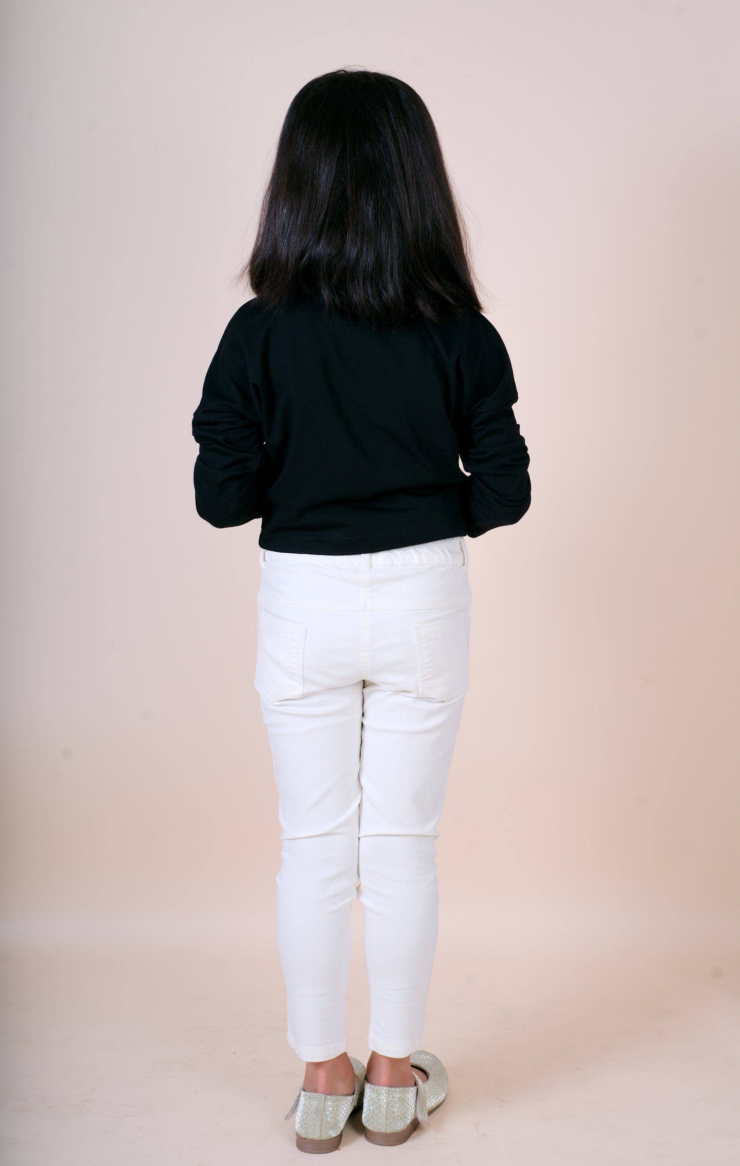A Girl wearing Little Carrot black top and white pants against a beige background