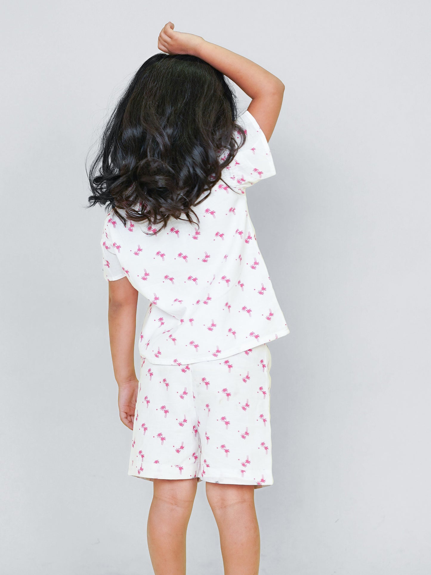 Little girl wearing a white cotton co-ord set with pink palm tree print, perfect summer playwear outfit by Little Carrot.