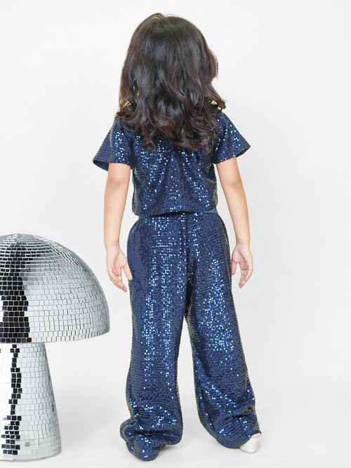 A little girl dazzles in a navy blue sequined co-ord set, featuring a chic crop top and straight pants with a glitter elastic waistband. Styled with shimmering shoes and surrounded by disco-inspired décor, this premium kids' wear ensemble is designed for a glamorous look with maximum comfort. Perfect for ages 3-14! ✨💙