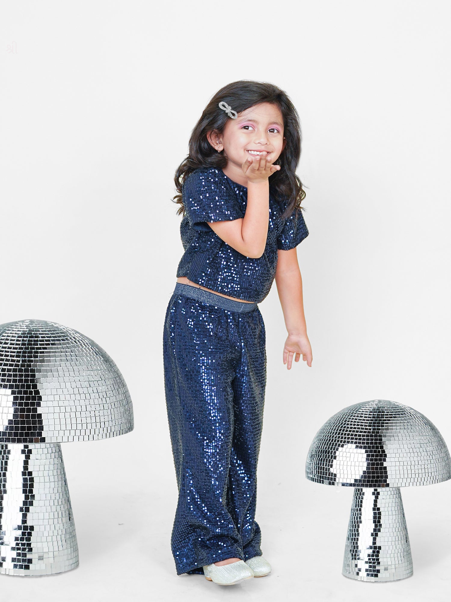 A little girl dazzles in a navy blue sequined co-ord set, featuring a chic crop top and straight pants with a glitter elastic waistband. Styled with shimmering shoes and surrounded by disco-inspired décor, this premium kids' wear ensemble is designed for a glamorous look with maximum comfort. Perfect for ages 3-14! ✨💙