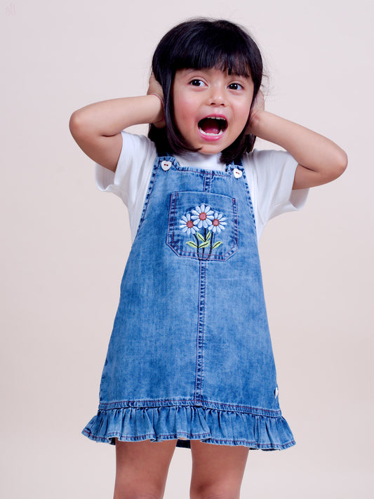 A stylish denim overall dress for infant and toddler girls, featuring floral embroidery on the front pocket, adjustable buttoned straps, and a ruffle hem for a cute and comfortable look.