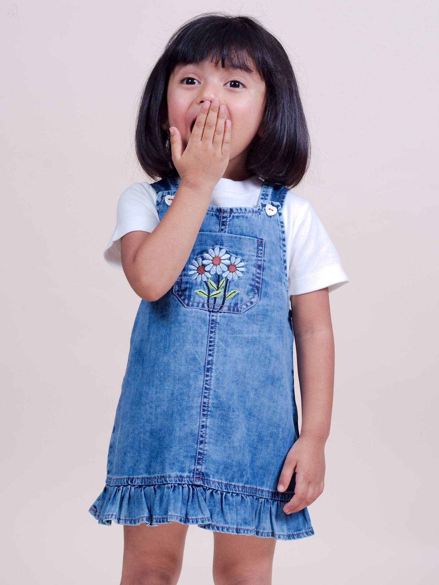 A stylish denim overall dress for infant and toddler girls, featuring floral embroidery on the front pocket, adjustable buttoned straps, and a ruffle hem for a cute and comfortable look.