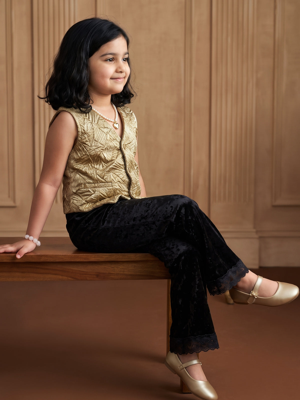 A young girl posing in Gold Vest paired with Black velvet pants from Pink Skies Collection by Little Carrot