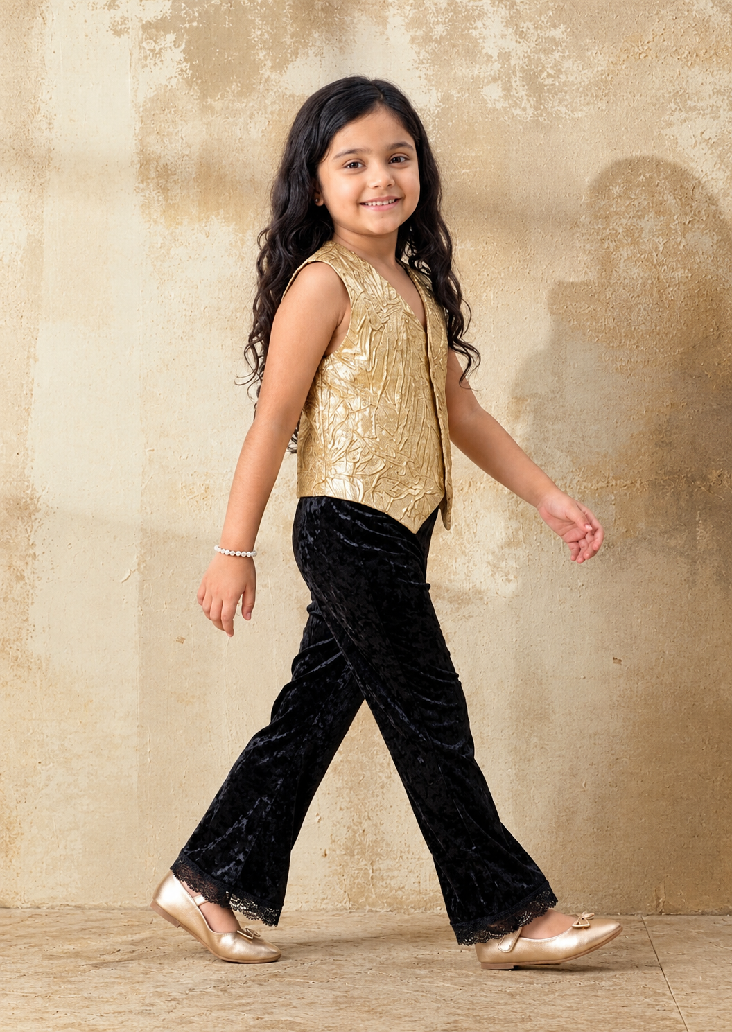 A young girl is posing in Gold vest and black velvet set from pink skies by Little Carrot
