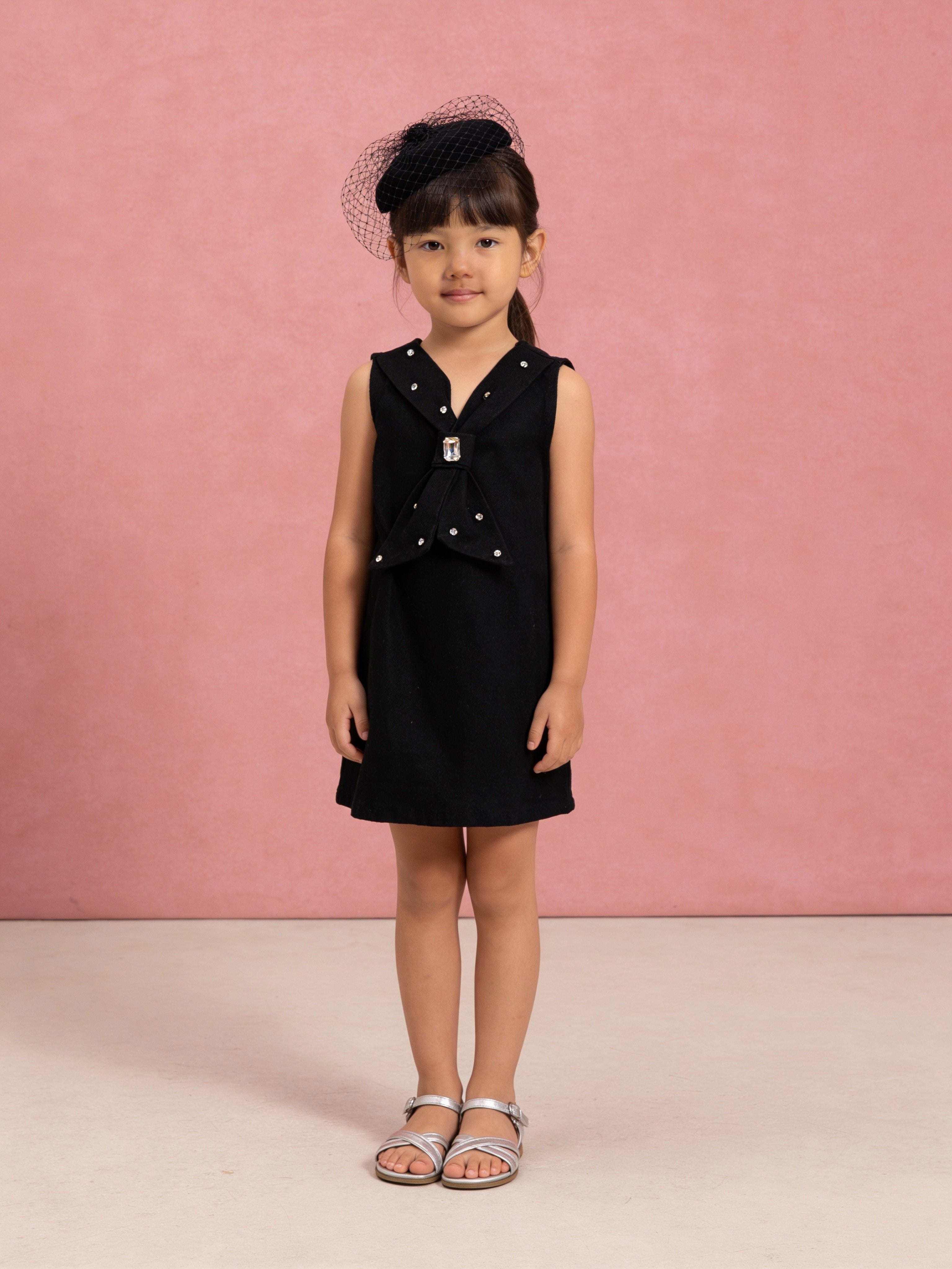Young girl wearing a Little Carrot Denim black dress with Hand Stitched Stone details against a pink background