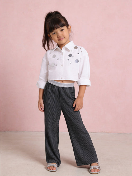 Young girl wearing a Little Carrot white cropped Shirt with Sequins Hilights paired with Silver Foil Printed Black Bottoms.