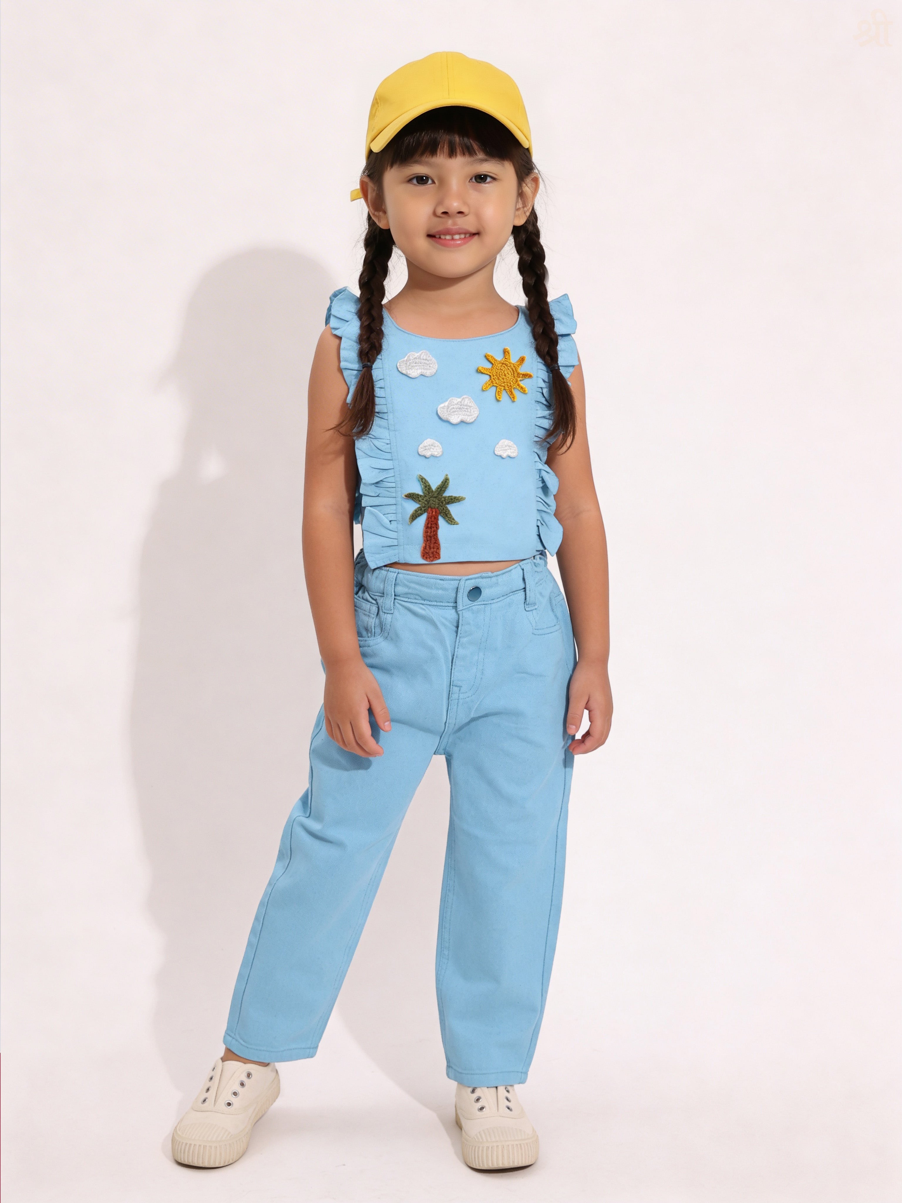 Child wearing a blue Little Carrot outfit with a sun and cloud handmade crochet patches, standing against a plain background