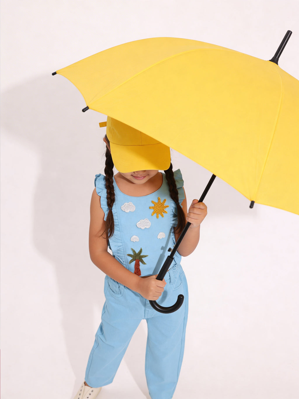 Child wearing a blue Little Carrot outfit with a sun and cloud handmade crochet patches, standing against a plain background