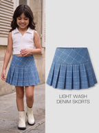 A child model wearing a light wash denim pleated skort with a white sleeveless top and white ankle boots, shown beside a product-only view of the skort on a light gray background with the text 'LIGHT WASH DENIM SKORTS'.