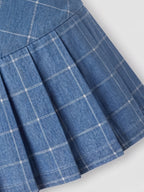 Close-up of a blue pleated skirt with a white windowpane plaid pattern, showing the fabric texture and stitching details.