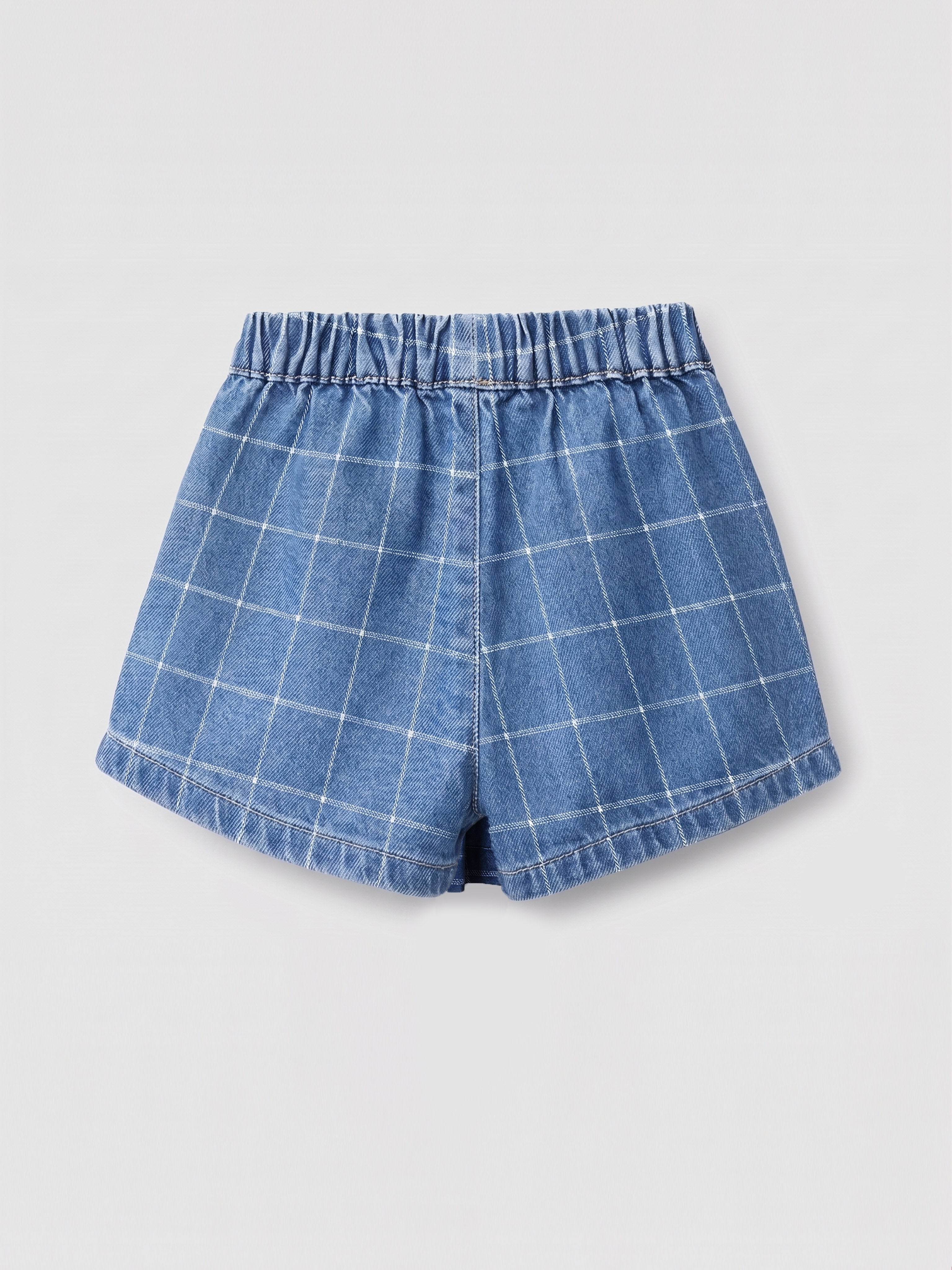 A pair of blue denim skorts with a white windowpane plaid pattern, featuring an elastic waistband, photographed flat on a light gray background.
