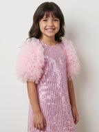 A young girl with dark brown hair smiling, wearing a Little Carrot light pink sequined dress with fluffy tulle puff sleeves, set against a plain off-white background.