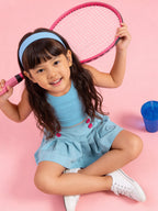 Young girl sitting in a little carrot blue co-ord set holding a pink tennis racket on a pink background
