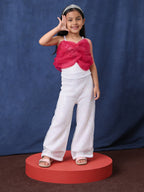 Young girl in a little carrot white sequins jumpsuit with a tiara, standing on a red platform against a blue background.