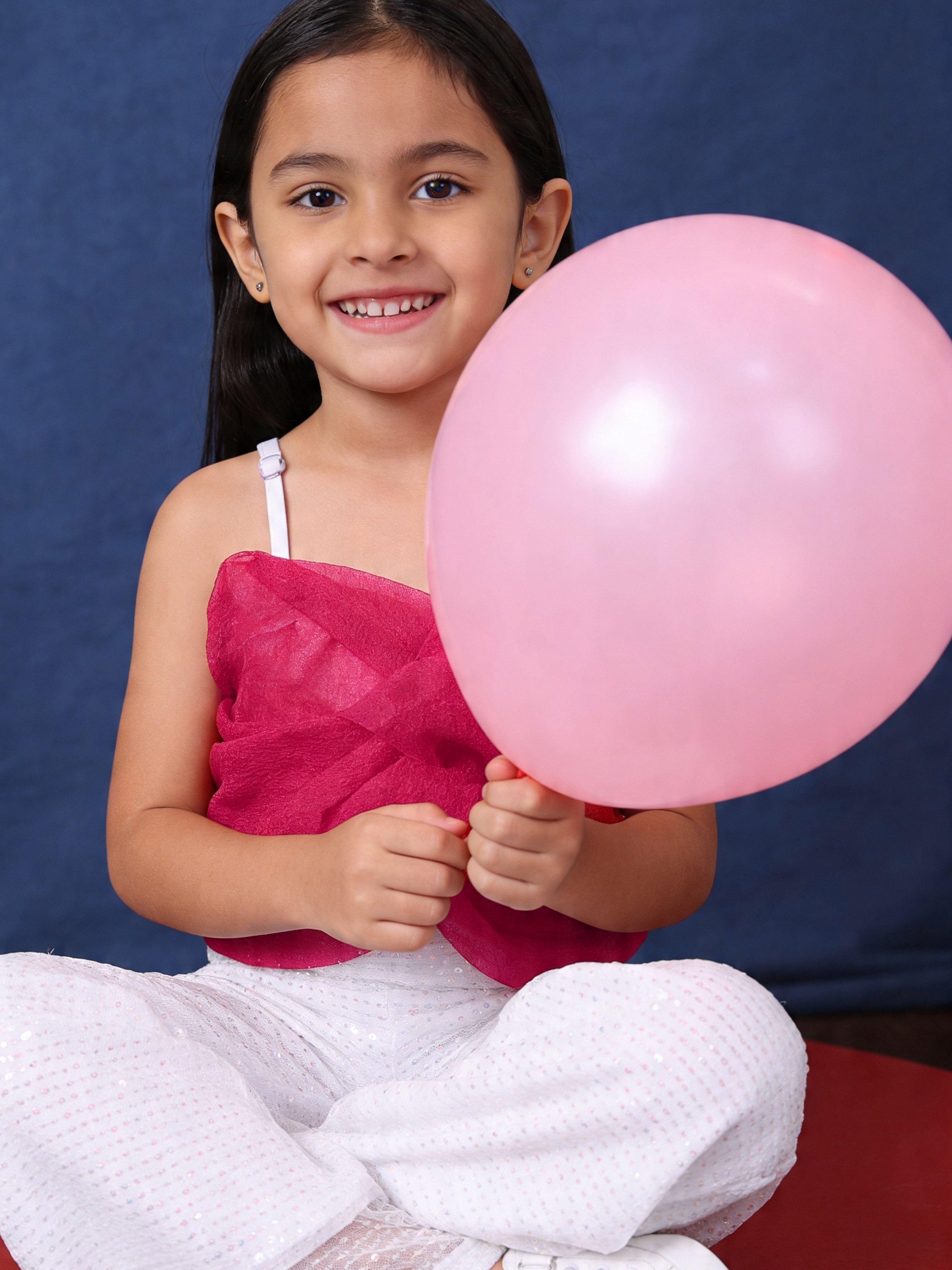 Young girl in little carrot partywear sequins jumpsuit,holding a pink balloon against a blue background