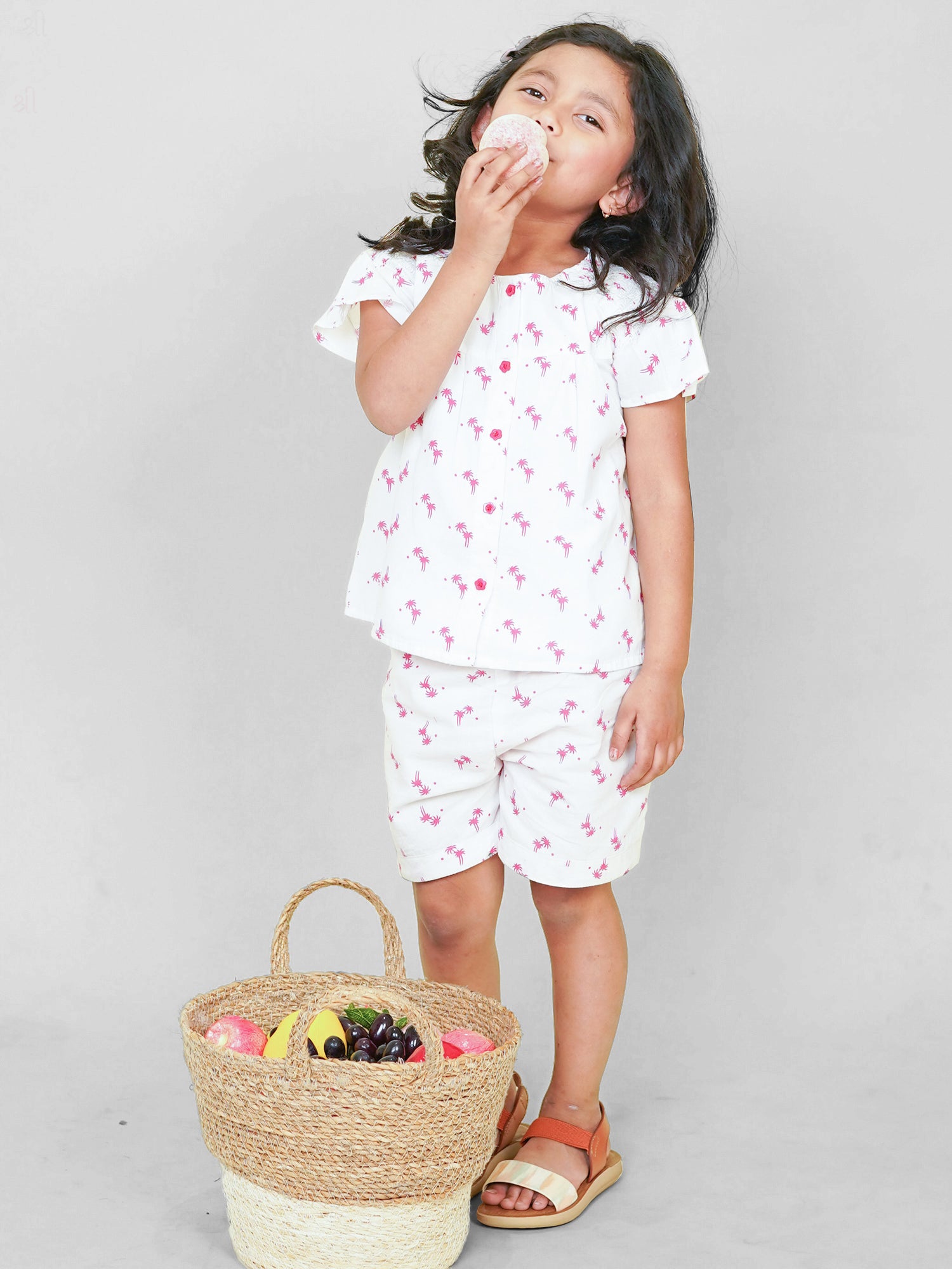 Little girl wearing a white cotton co-ord set with pink palm tree print, perfect summer playwear outfit by Little Carrot.
