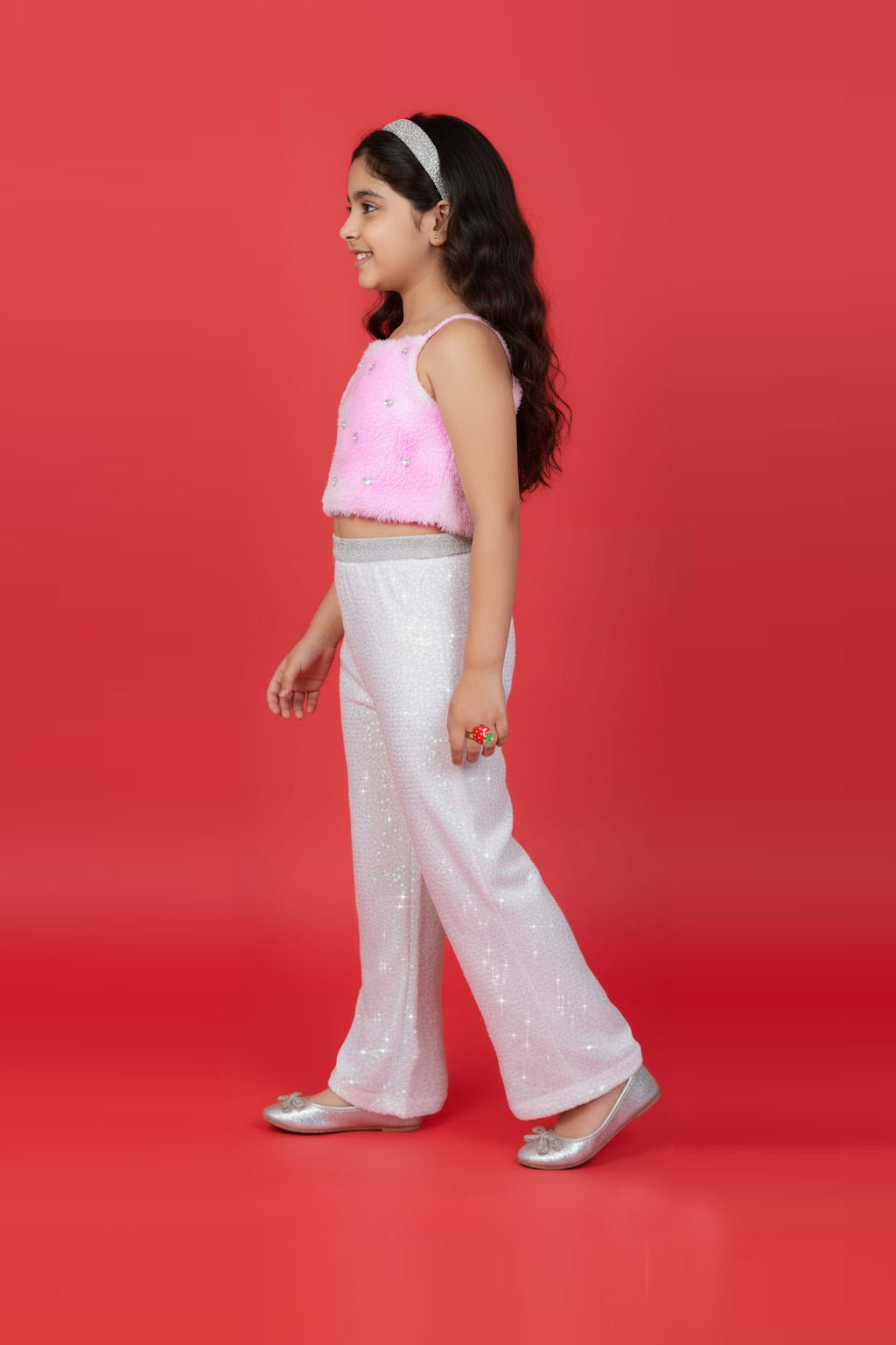 A Girl wearing a Little Carrot Partywear Fur top and white sequin pants on a red background with disco balls.