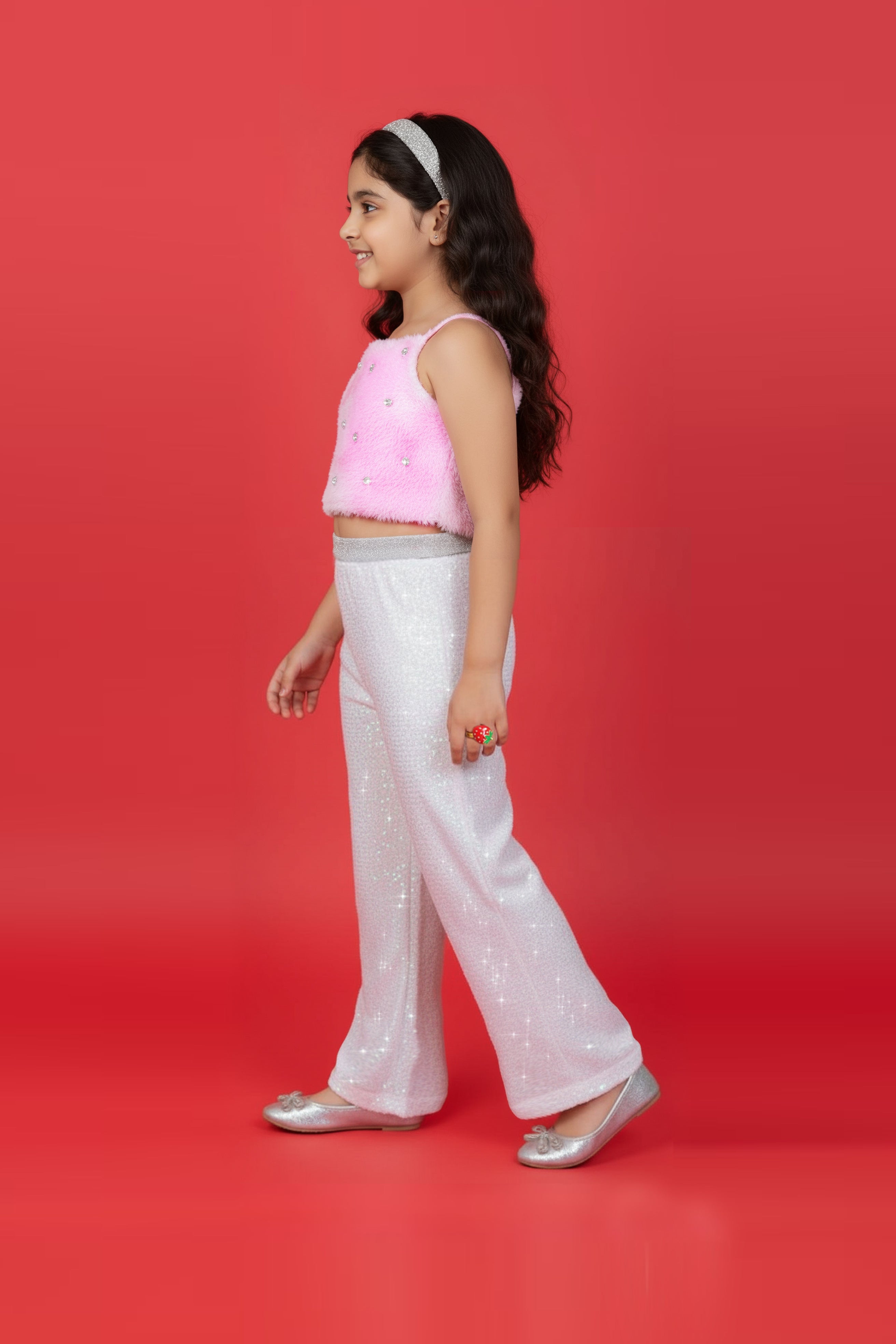 A Girl wearing a Little Carrot Partywear Fur top and white sequin pants on a red background with disco balls.