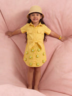Child wearing a Little Carrot yellow Shirt  dress with floral embellishments on a pink background