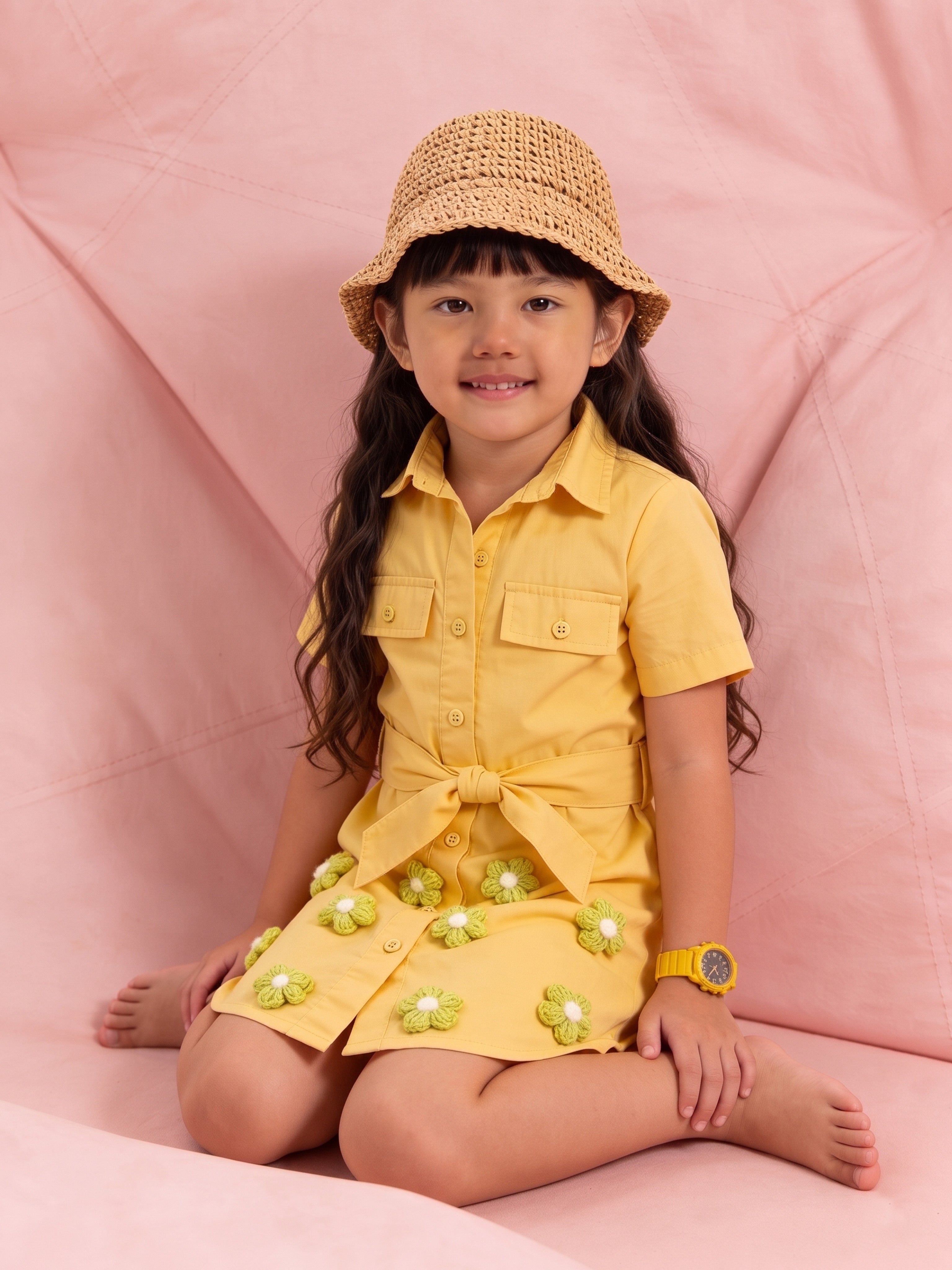 Young girl in a yellow little carrot outfit with a straw hat sitting on a pink surface