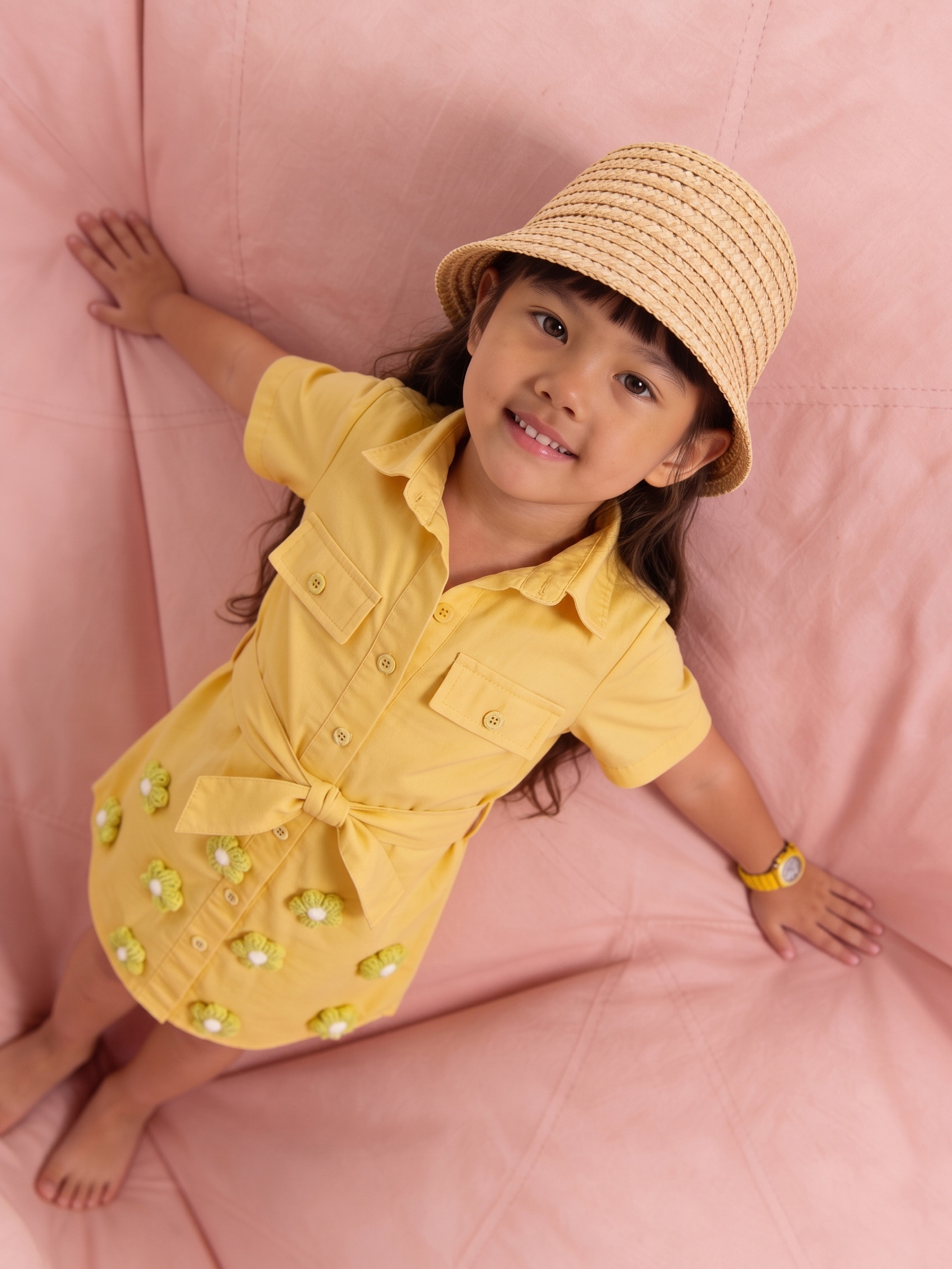 Child wearing a yellow little carrot dress with a bow and a straw hat on a pink background