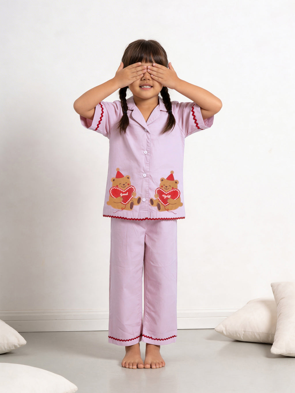 Girl wearing little carrot pink pajamas night suit with bear designs, standing against a white background.