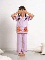 Girl wearing little carrot pink pajamas night suit with bear designs, standing against a white background.