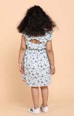 Smiling girl wearing a white floral summer dress with frill sleeves and handmade flower detail at the chest, designed by Little Carrot.