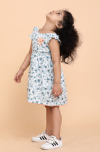 Smiling girl wearing a white floral summer dress with frill sleeves and handmade flower detail at the chest, designed by Little Carrot.