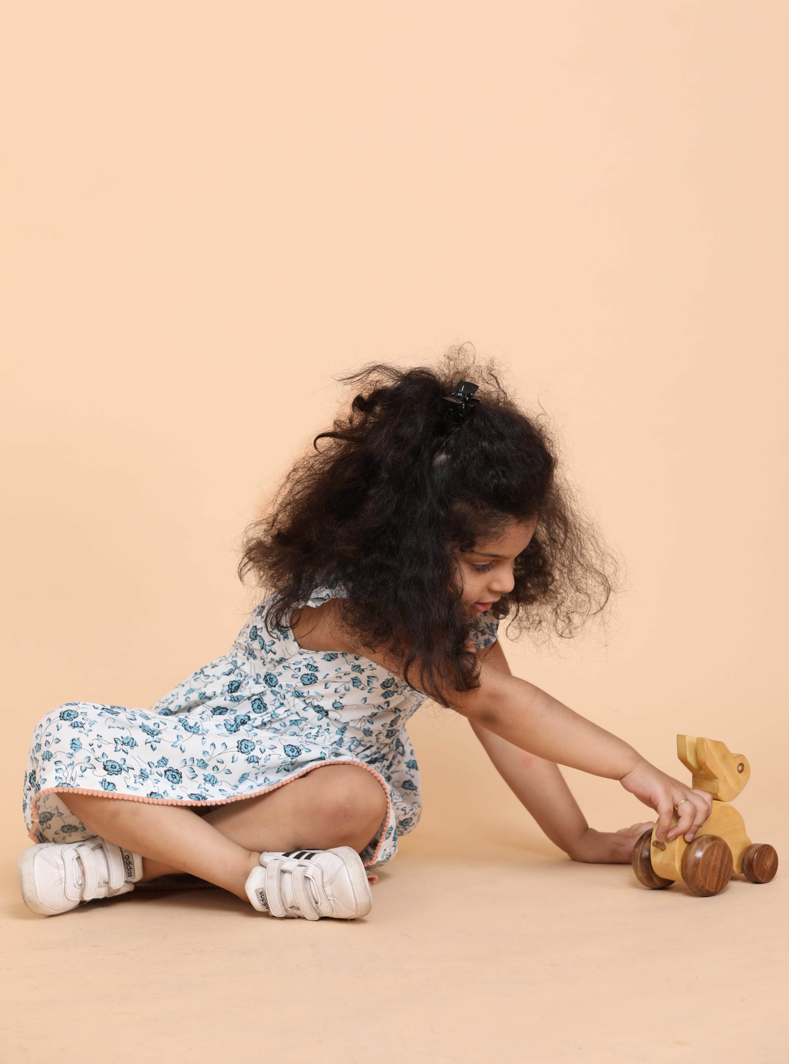 Smiling girl wearing a white floral summer dress with frill sleeves and handmade flower detail at the chest, designed by Little Carrot.